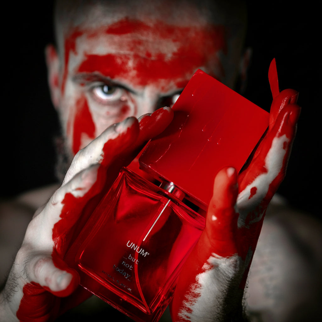 Red Unum perfume bottle held by a person with red and white makeup.