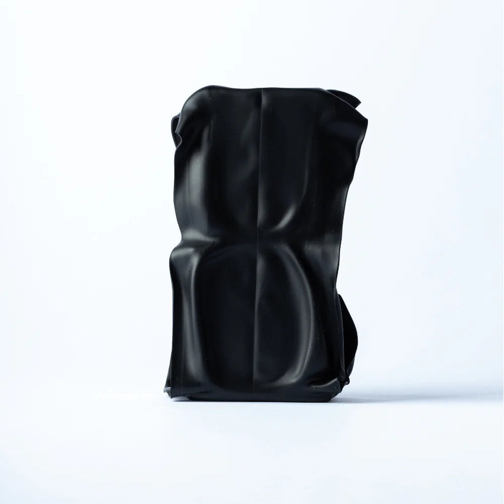 A black sculptural shoulder bag with a glossy, dimpled texture, standing upright on a clean white studio background.