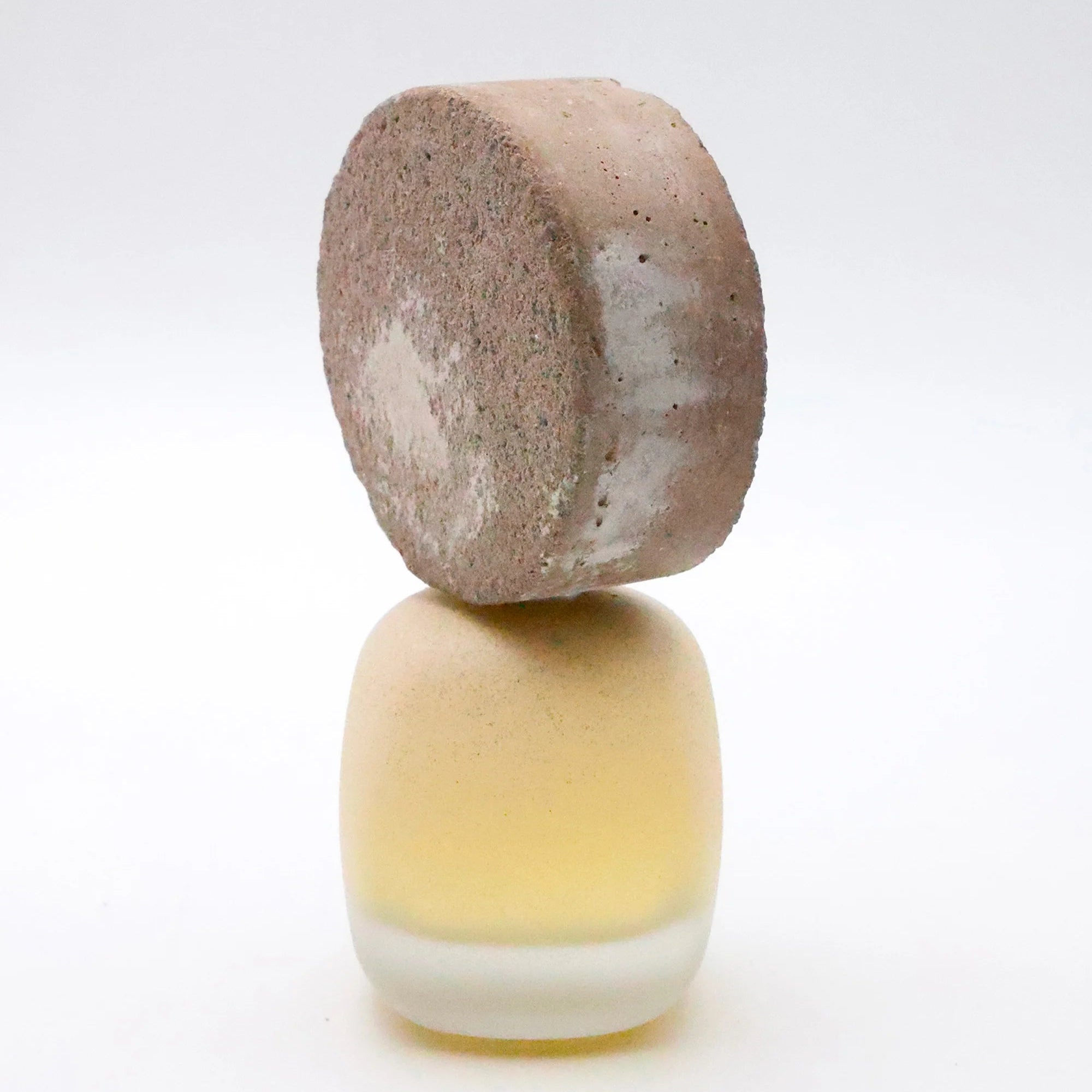 A small decorative object featuring a round, textured brown top resting on a rounded, frosted pale yellow and white base, photographed against a seamless white background.