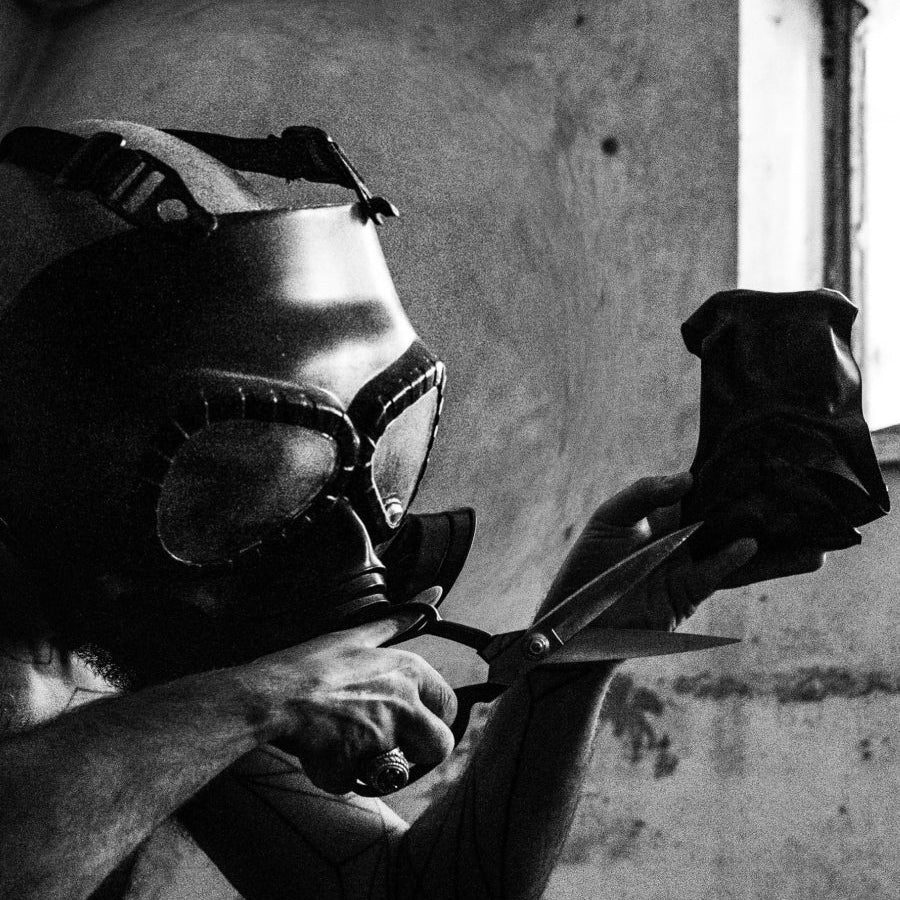 Person wearing a welding helmet and gloves holding a pair of scissors in a workshop.